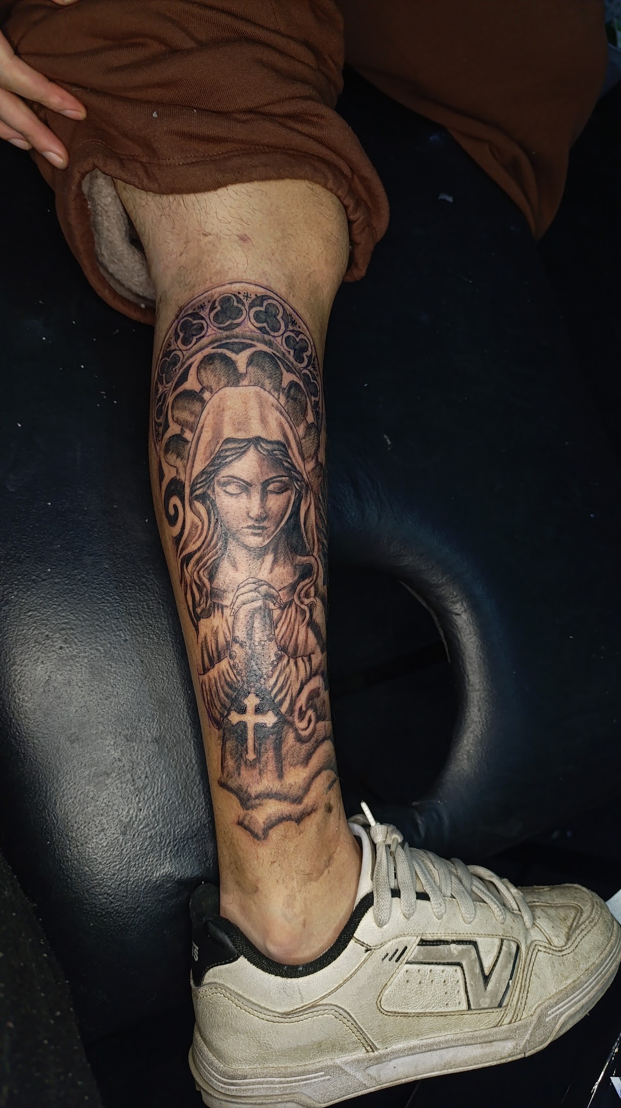 Tatuaje religioso Black and Grey de la Virgen con rosario en la pierna, por Ares Tattoo